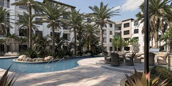 A pool surrounded by palm trees and chairs at The Stadler Luxury Apartments, Bradenton, Florida